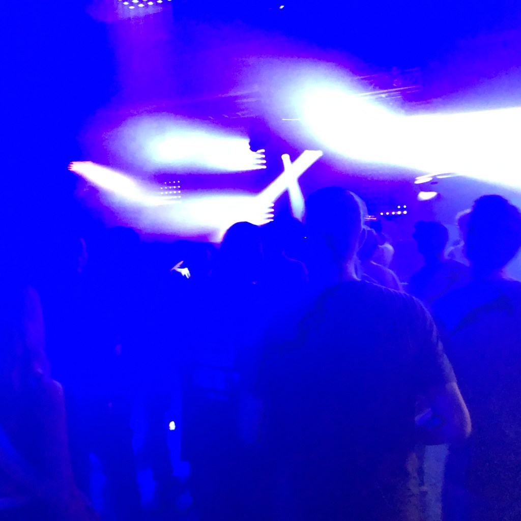Blue lights cut through with layers in a rave, silhouettes dances agains the club lights.

